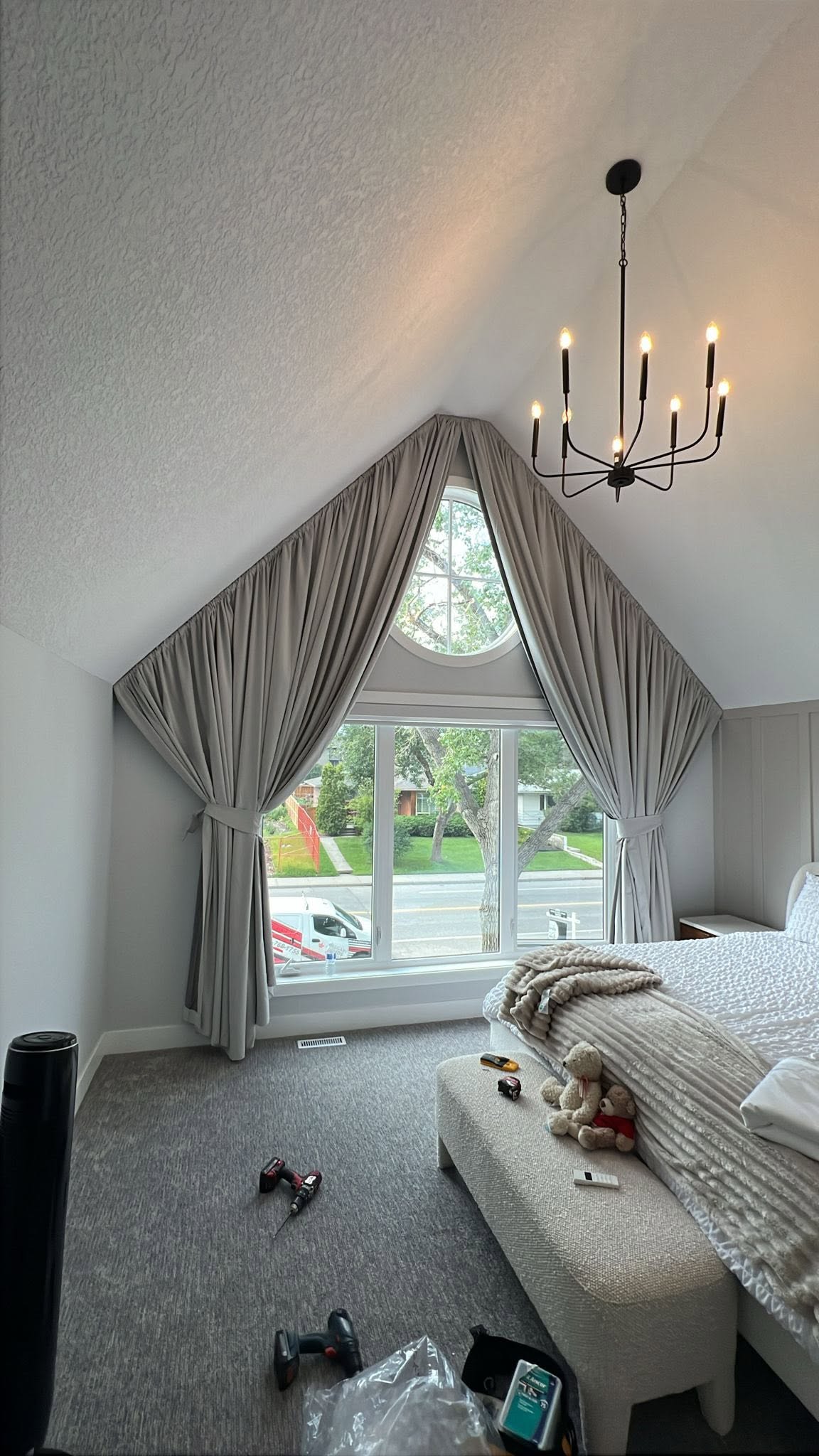 Custom drapery following the roofline of a vaulted gable bedroom, with a round window at the apex, in a Calgary home